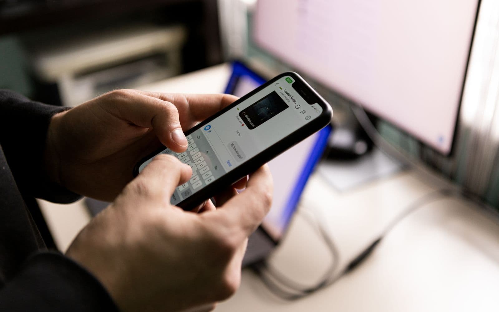 A person typing a message on a smartphone at a desk